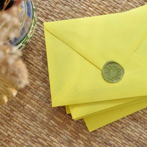Een handgemaakte vaas met bloemen, en gele enveloppen met de herkenbare groene zonnebloem stempel wat onderdeel is van de branding van Claudia Carreiro Contentstrategie